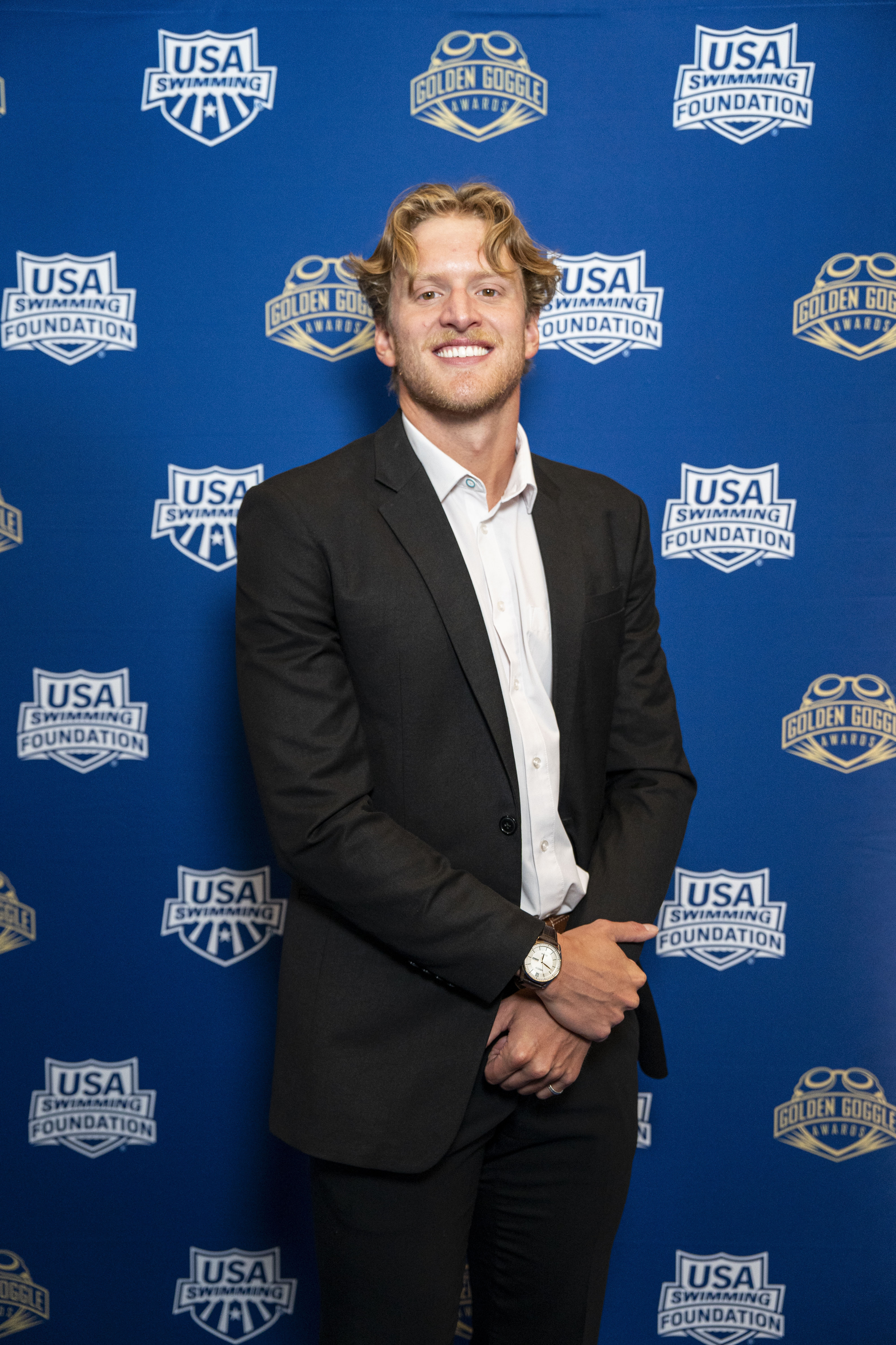 Grant House in a black suit at the Golden Goggles awards, against a blue backdrop