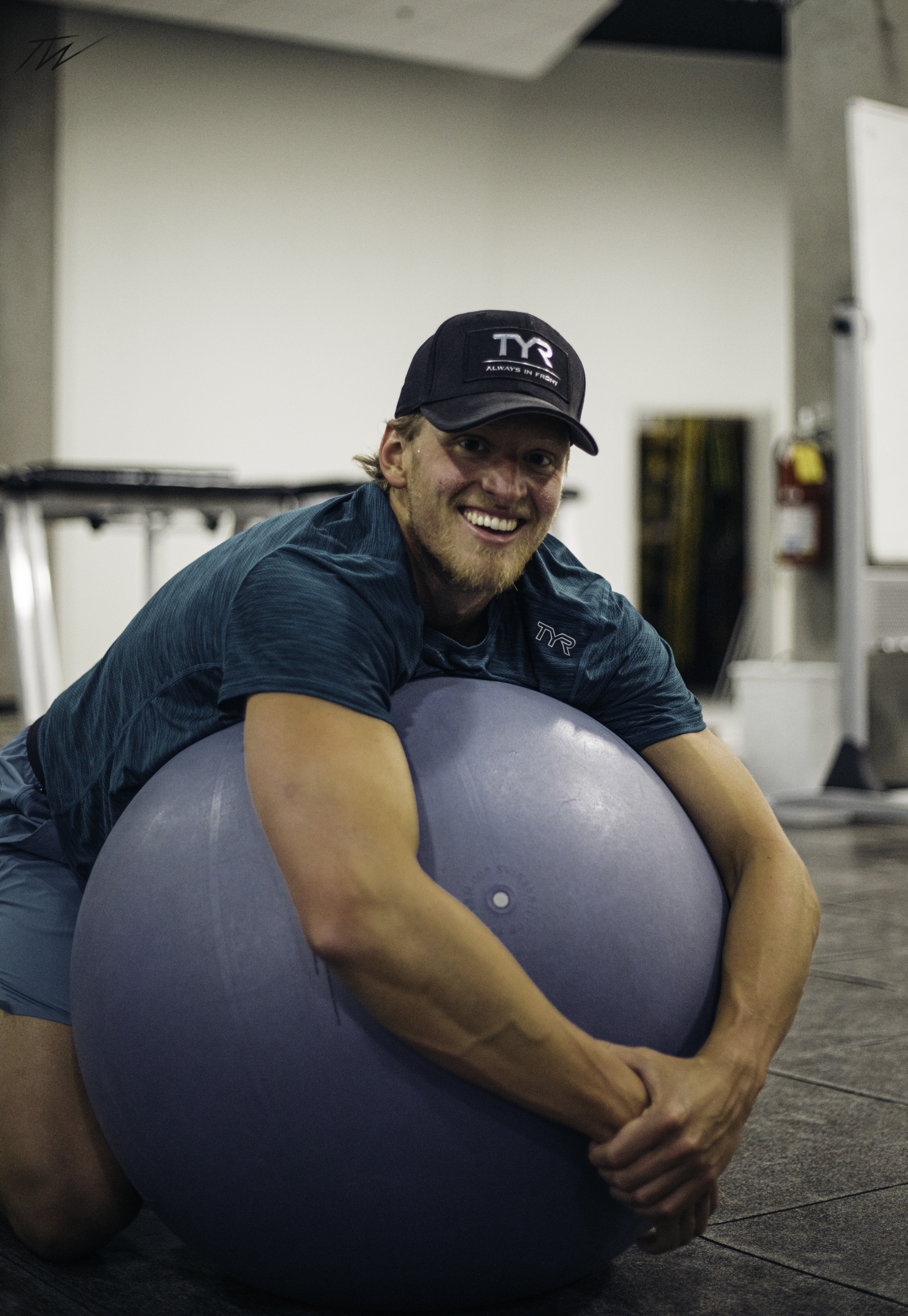 Grant House wearing a cap and leaning over an exercise ball in a training space